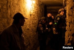 Một người đàn ông đứng cạnh các thành viên cảnh sát Ukraine trong hầm trú ẩn dưới lòng đất sau khi một cuộc tấn công phi đạn làm hư hại một tòa nhà chung cư, ở Dobropillia, thuộc vùng Donetsk, Ukraine, ngày 30 tháng 4 năm 2022.