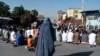 Seorang perempuan Afghanistan berpakaian burqa berdiri ketika umat Muslim melakukan salat Idulfitri, yang menandai berakhirnya bulan suci Ramadhan di luar sebuah masjid di sebuah jalan di Kabul pada 1 Mei 2022. (Foto: AFP/Wakil Kohsar)