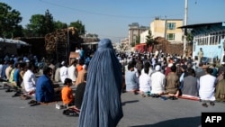 Seorang perempuan Afghanistan berpakaian burqa berdiri ketika umat Muslim melakukan salat Idulfitri, yang menandai berakhirnya bulan suci Ramadhan di luar sebuah masjid di sebuah jalan di Kabul pada 1 Mei 2022. (Foto: AFP/Wakil Kohsar)