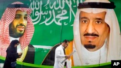 FILE - People walk past a banner showing Saudi King Salman, right, and Crown Prince Mohammed bin Salman, outside a mall in Jiddah, Saudi Arabia, March 7, 2020. 