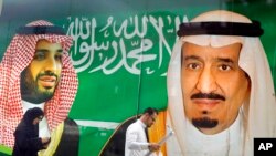 FILE - People walk past a banner showing Saudi King Salman, right, and Crown Prince Mohammed bin Salman, outside a mall in Jiddah, Saudi Arabia, March 7, 2020. 