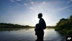FILE - A father carries his daughter over the Rio Grande river toward Del Rio, Texas, from Ciudad Acuna, Mexico, Sept. 22, 2021. 