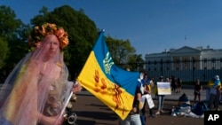 A demonstrator, dressed in a wedding dress with gas masks and holding Ukraine's flag with red-paint stains representing Ukrainian deaths, walks during a protest in solidarity with Ukraine outside the White House in Washington, April 23, 2022.