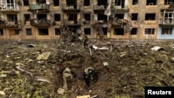 Ukrainian military personnel inspect the site of a missile strike in front of a damaged residential building in Dobropillia, in the Donetsk region, Ukraine, April 30, 2022.