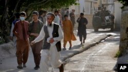 People leave the site of an explosion at a mosque as a Taliban fighter stands guard, in Kabul, Afghanistan, April 29, 2022. A second mosque was targeted in Kabul on Saturday.