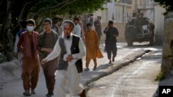 La gente abandona el lugar de una explosión en una mezquita mientras un combatiente talibán hace guardia, en Kabul, Afganistán, el 29 de abril de 2022.