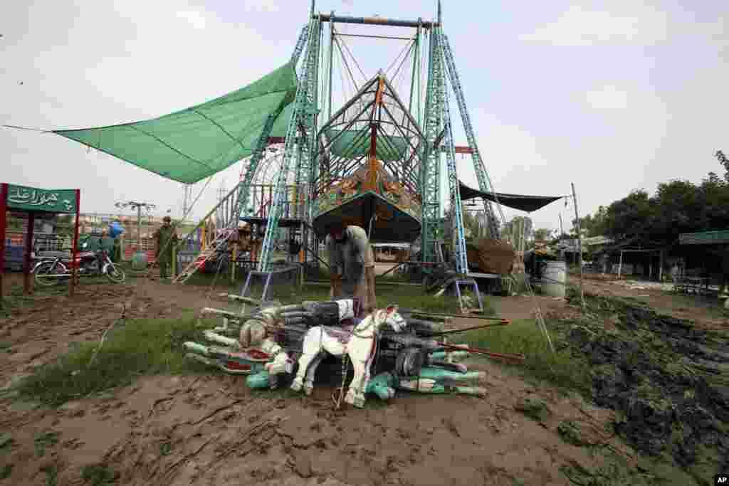An amusement park worker collects parts of a swinging horse ride after it was damaged by heavy rain, in Charsadda, Pakistan, Sept. 5, 2022.