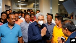 In this handout picture provided by the Ministry of Urban Development and Housing of Government of Sri Lanka, Sri Lanka's former President Gotabaya Rajapaksa, wearing mask, is greeted upon his arrival at Bandaranaike International airport in Colombo, Sri 