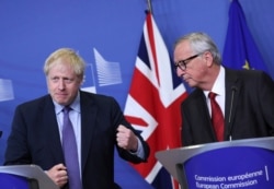 FILE - British Prime Minister Boris Johnson gestures as he stands alongside European Commission President Jean-Claude Juncker during a press point at EU headquarters in Brussels, Oct. 17, 2019.