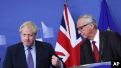 FILE - British Prime Minister Boris Johnson gestures as he stands alongside European Commission President Jean-Claude Juncker during a press point at EU headquarters in Brussels, Oct. 17, 2019. 