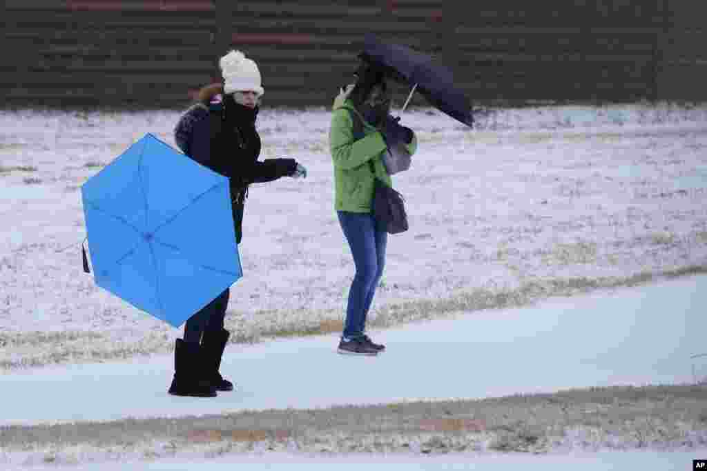Amanda, a la izquierda, y Rebecka intentan usar paraguas mientras caminan al trabajo durante una lluvia helada.
