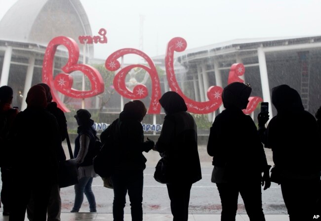 Sejumlah warga berlindung dari hujan setibanya di Bandara Internasional Bali, pada Jumat, 4 Februari 2022. (Foto: AP)