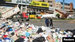 People walk past piled up garbage as trucks block a highway during a protest by Land Transport Unions against worsening economic conditions, in Dora, Lebanon Feb. 2, 2022. 