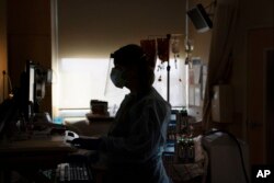 FILE - A registered nurse works on a computer while assisting a COVID-19 patient in Los Angeles. Many American hospitals are looking abroad for health care workers, saying they're facing a dire shortage of nurses amid the slogging pandemic.