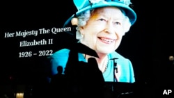 FILE - People pass by an image of Queen Elizabeth II projected onto a large screen at Piccadilly Circus, in London, Sept. 8, 2022. 