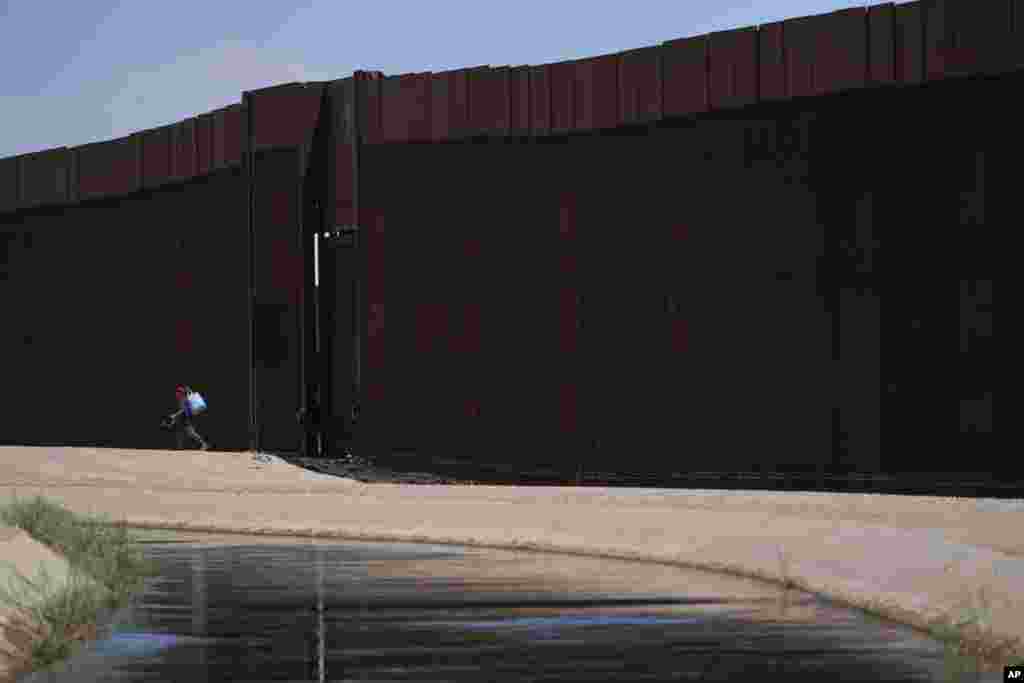 FILE - A man walks between a canal carrying water from the Colorado River and a border wall separating San Luis Rio Colorado, Mexico with San Luis, Ariz., on Sunday, Aug. 14, 2022, in San Luis Rio Colorado, Mexico. 