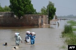 Flood-affected people wade through a flooded area with relief food bags as they return to their homes on the outskirts of Jacobabad, Sindh province, Sept. 6, 2022.