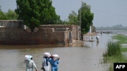 Sejumlah warga berjalan melintasi area yang tergenang banjir di pinggiran kota Jacobabad, Pakistan, pada 6 September 2022. Mereka berjalan pulang kembali ke rumah dengan membawa bantuan makanan. (Foto: AFP/Aamir Qureshi)