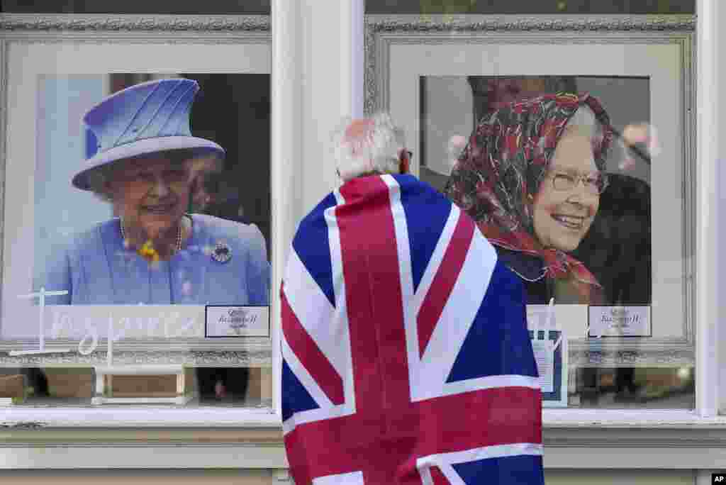 A man looks at framed portraits of Queen Elizabeth II in a shop window near Windsor Castle in Windsor, England.