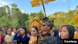 Sepasang pengantin remaja berbaju adat berjalan sambil dipayungi para warga desa. (Courtesy: Ilsa Diasty)
