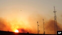 FILE- A helicopter carries water on a longline to a wildfire near Salem, Ore., at sunset Sept. 9, 2022. 