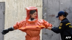A Ukrainian Emergency Ministry rescuer assists a woman to put on protective clothing during a nuclear emergency training session for civilians in the western Ukrainian city of Lviv on Sept. 8, 2022.
