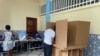 Eleitora na fila para votar, enquanto outro vota no cubículo de uma assembleia de voto em Luanda. Angola