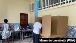 Eleitora na fila para votar, enquanto outro vota no cubículo de uma assembleia de voto em Luanda. Angola