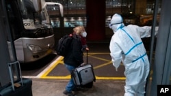 FILE - A passenger is directed to a bus by an Olympic worker wearing protective gear at the Beijing Capital International Airport ahead of the 2022 Winter Olympics in Beijing, Jan. 24, 2022. 