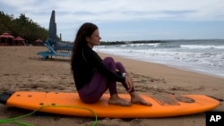 A Russian tourist sits on her surfboard as she watches waves at Kuta beach, Bali, Indonesia on Friday, Feb. 4, 2022. (AP Photo/Firdia Lisnawati)