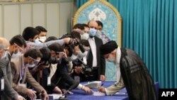 Pemimpin Tertinggi Iran Ayatollah Ali Khamenei disambut oleh pekerja pemilihan, semuanya mengenakan masker wajah karena pandemi COVID-19, saat ia tiba untuk memberikan suaranya pada 18 Juni 2021. (Foto: AFP)