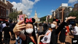 Visitors wearing face masks to prevent the spread of the new coronavirus, take a selfie at the Hong Kong Disneyland on Thursday, June 18, 2020. Hong Kong Disneyland on Thursday opened its doors to visitors for the first time in nearly five months,…
