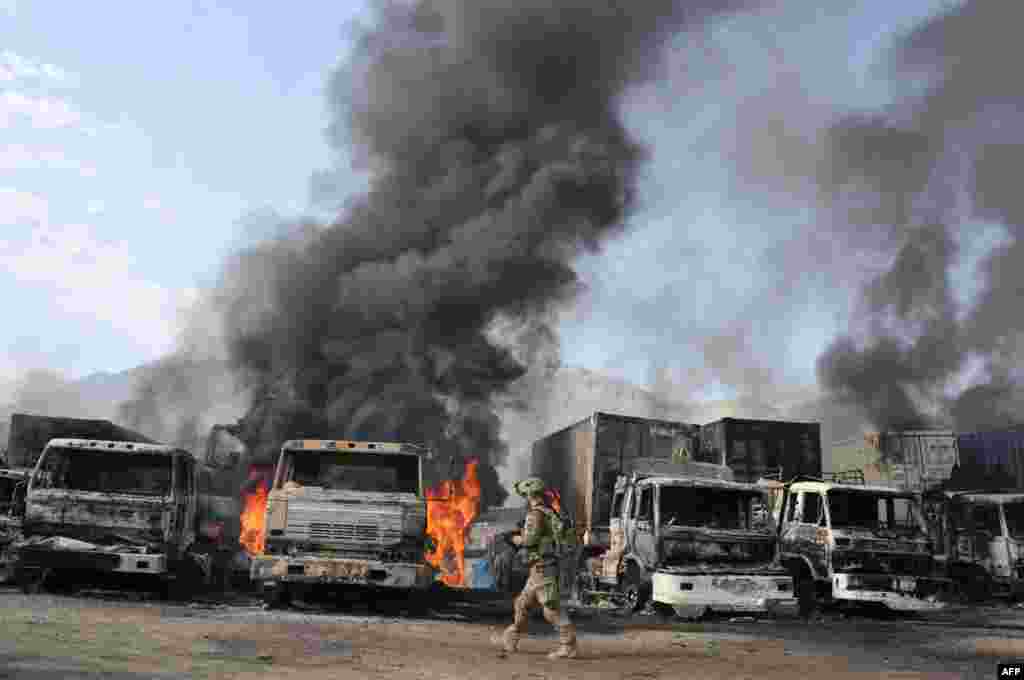 A U.S. soldier walks past burning trucks at the scene of a suicide attack at the Afghan-Pakistan border crossing in Torkham, Nangarhar province.