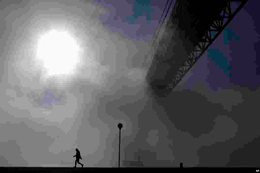 A man walks near the April 25th bridge by the Tagus riverbank in Lisbon, Portugal, on a foggy morning.