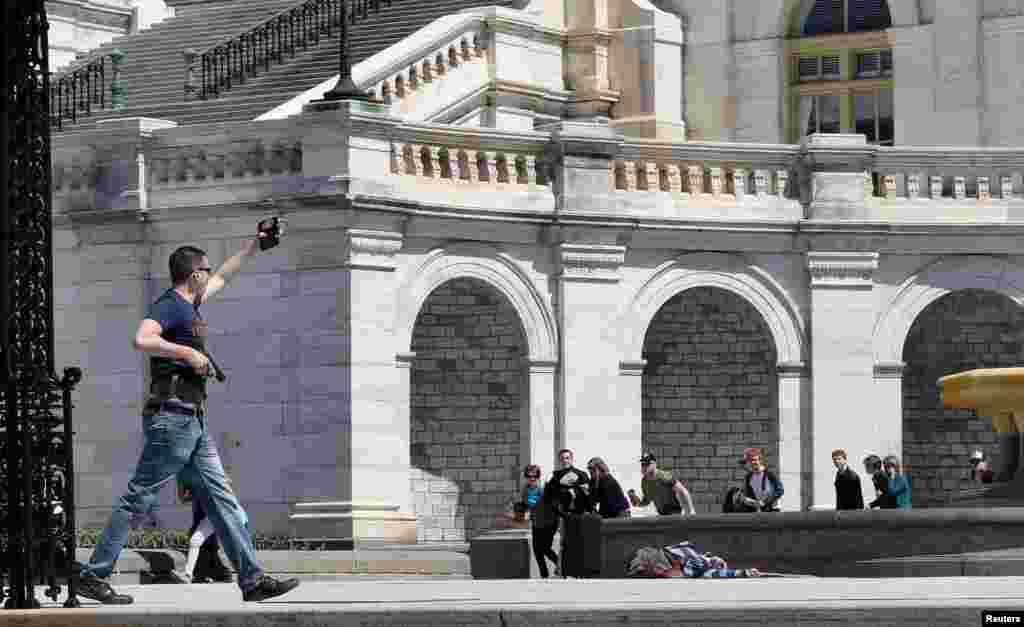 Di foto yang baru dipublikasikan hari ini, seorang polisi menunjukkan lencananya kepada para turis ketika mendekati seorang pria yang bunuh diri di depan gedung Kongres di Washington D.C., 11 April 2015. Seorang pria menembak mati dirinya dekat gedung Kongres AS, kata polisi, menyebabkan polisi menutup wilayah tersebut di salah satu hari paling ramai dikunjungi turis di Washington.