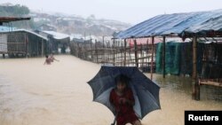 ရေကြီးနေတဲ့ ကူတူပလောင် ဒုက္ခသည်စခန်းထဲ ဖြတ်ကူးလာနေသည့် ရိုဟင်ဂျာကလေးမလေးတဦး။ (ဇူလိုင် ၄၊ ၂၀၁၈)