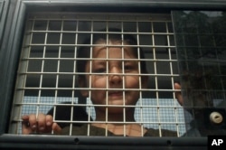 FILE - Ethnic Uighur Muslim boy stands inside a police van in Khlong Hoi Khong of southern Songkhla province, Thailand, March 15, 2014. He was in a group of 200 people rescued from a human trafficking camp.