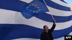 A man waves an European flag in front of giant Greek one, during a pro-European demonstration in front of the Greek parliament in Athens on June 22, 2015. 