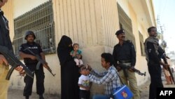 Pakistani policeman stand guard as a health worker administers polio drops to a child during a polio vaccination campaign after a day of an attack by gunmen in Karachi on April 21, 2016.