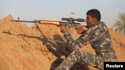 File - A Shiite fighter takes aim during a patrol in Jurf al-Sakhar, Iraq, which Iraqi security forces retook from Islamic State militants, Oct. 25, 2014. 