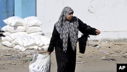 A Palestinian woman drags a sack of flour received as food supplies at a United Nations food aid distribution center, Shati refugee camp, Gaza City. (file photo)