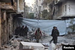 Syrian government soldiers walk amid rubble of damaged buildings after they took control of al-Sakhour neighborhood in Aleppo, in this handout picture provided by SANA, Nov. 28, 2016.