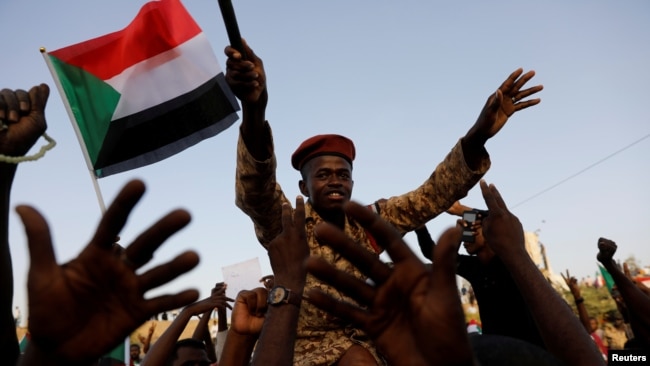 A Sudanese soldier sits on the shoulders of a demonstrator, cheering with the crowd outside Defense Ministry in Khartoum, Sudan, April 16, 2019.