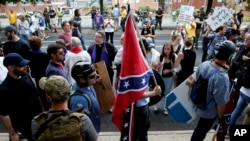 Seorang pendukung supremasi kulit putih membawa bendera Konfederasi saat berjalan melewati demonstran dari kelompok penentang rasisme di Charlottesville, Virginia, Aug. 12, 2017. 