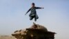 An Afghan boy jumps from the remains of a Soviet-era tank on the outskirts of Jalalabad, Afghanistan, Feb. 15, 2019. 