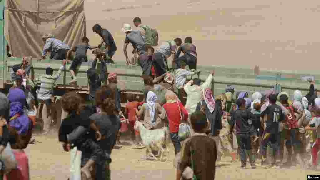 Displaced people from the minority Yazidi sect jump onto a truck as they make their way toward the Syrian border town of Elierbeh of Al-Hasakah Governorate, Aug. 10, 2014. 