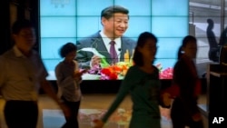People walk past a large videoscreen showing Chinese President Xi Jinping during his trip to the United States from Chinese state broadcaster CCTV in an office building in Beijing, Sept. 25, 2015.