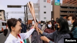 FILE PHOTO: Spectators try to touch the torch carried by torchbearer Junko Ito, after her run during the Tokyo 2020 Olympic torch relay on the second day of the relay in Fukushima, Japan March 26, 2021. REUTERS/Issei Kato/File Photo