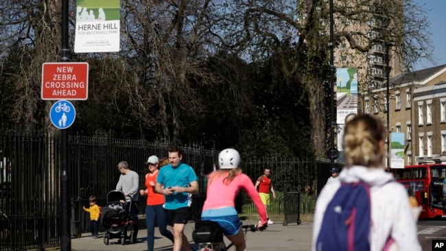 Las personas observan el distanciamiento social cuando pasan por las puertas cerradas del Parque Brockwell en Londres, cerrado durante la noche por el consejo local para ayudar a detener la propagación del coronavirus.