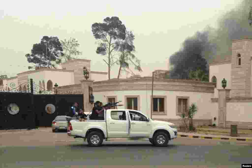Armed men aim their weapons as smoke rises in the background near the General National Congress, in Tripoli, May 18, 2014. 